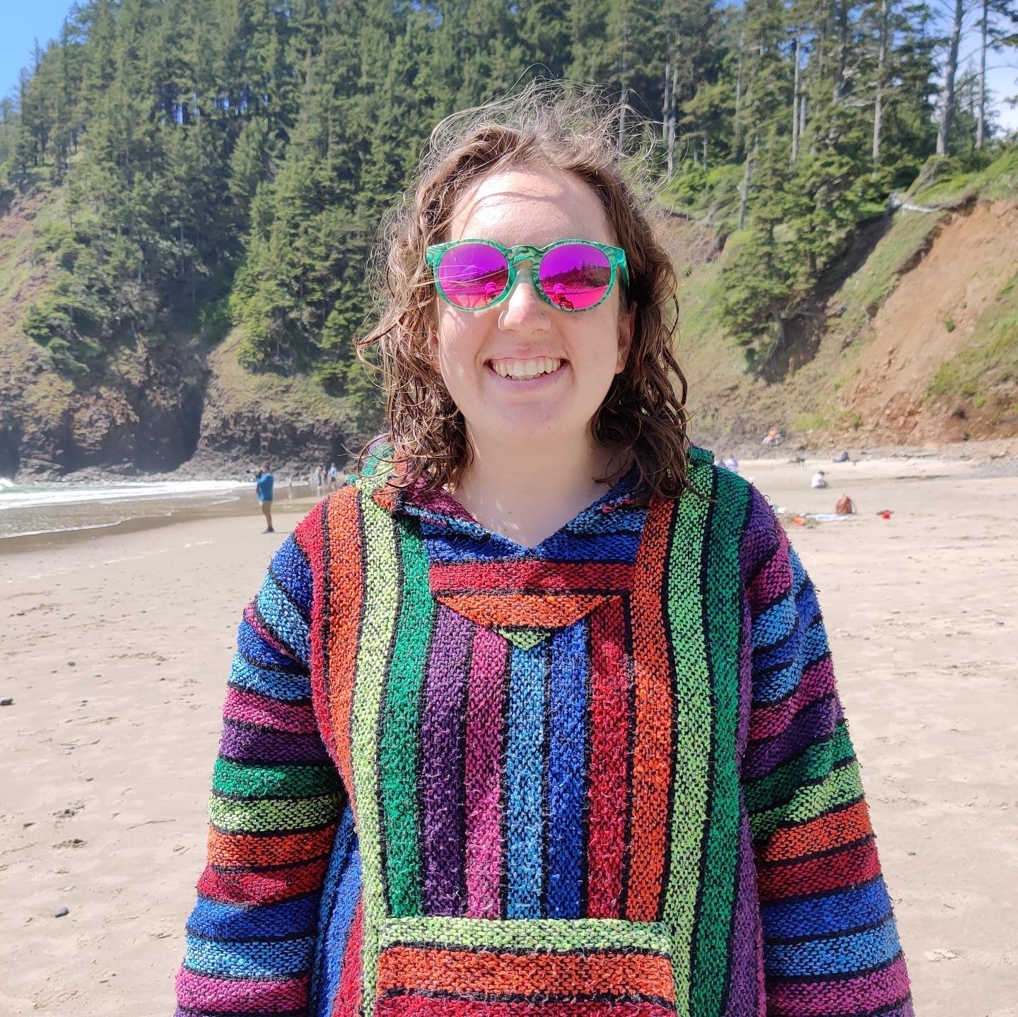 A picture of me wearing a rainbow hoodie on an Oregon beach